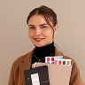 Smiling woman holding color swatches in one hand, wearing brown jacket and black turtleneck.